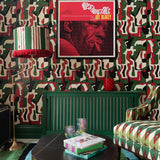 A closer view of a red, green and black abstract face print wallpaper behind a red-fringed lamp and green radiator, framed Art Blakey poster above.