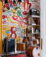Music room with drum kit, amps, guitar, bookshelf, and colourful music-themed graffiti-style wallpaper.