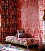 A maximalist bedroom setting with vivid pink and orange wallpaper, matching patterned curtains, and a fringed daybed with tropical motifs, creating a warm, exotic atmosphere.