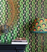 A bold green geometric wallpaper is paired with a gold sunburst mirror, an ornate crown, and a striking fringed lampshade.