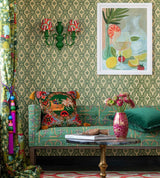 A vibrant living room with Palloncini Verde wallpaper, a green patterned sofa, bold cushions, floral décor, and a framed citrus-inspired painting