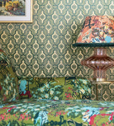 A cozy corner featuring Palloncini Verde wallpaper, a green botanical-patterned sofa, and a statement glass lamp with a floral lampshade.