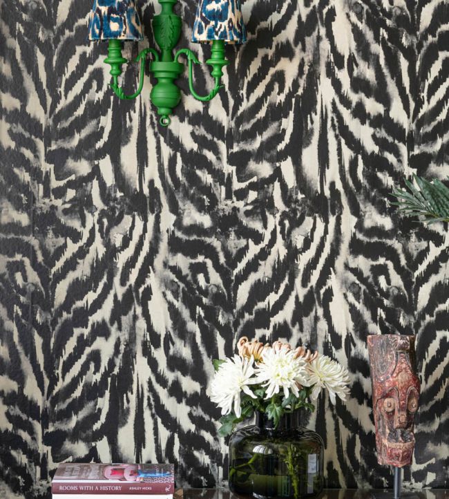 A close-up of Zebrato Nero wallpaper by Mind The Gap, paired with a vibrant green wall sconce, fresh flowers, and eclectic decorative accents