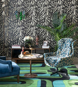 A bold living space featuring Zebrato Nero wallpaper by Mind The Gap, a plush blue armchair, a leopard-print swivel chair, and lush greenery
