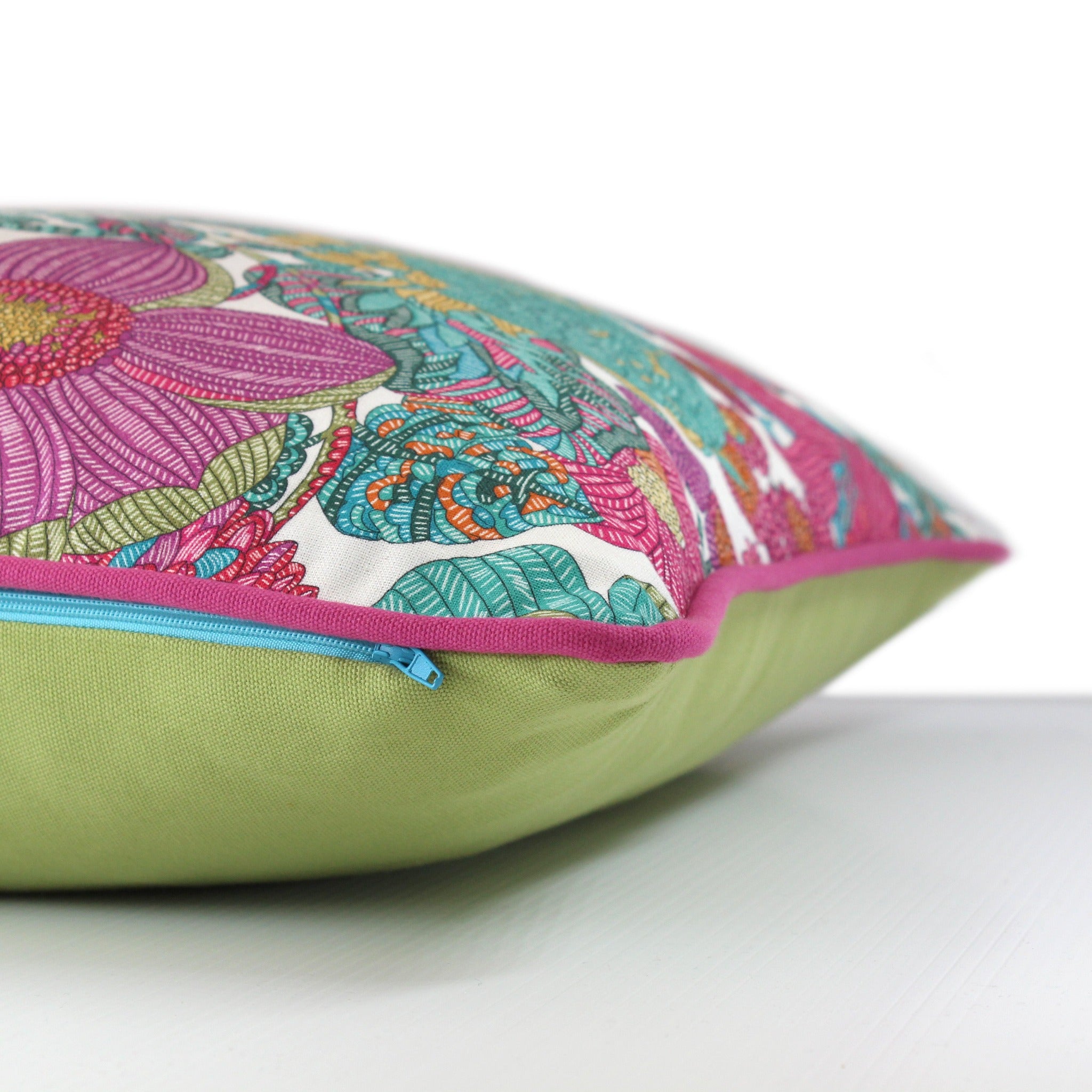 Side view of a bright colourful floral cushion with retro inspired flowers in hot pink, grape, bright turquoise, coral and orange with fuschia piping and a caper green cotton back