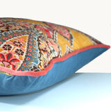 Sideshot of a cushion with a sky blue velvet back, pink velvet piping and ornate paisley design on front with mustard background.