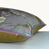 Side shot of a cushion with a grey background and pink, blue and lilac flowers and olive vine like leaves.