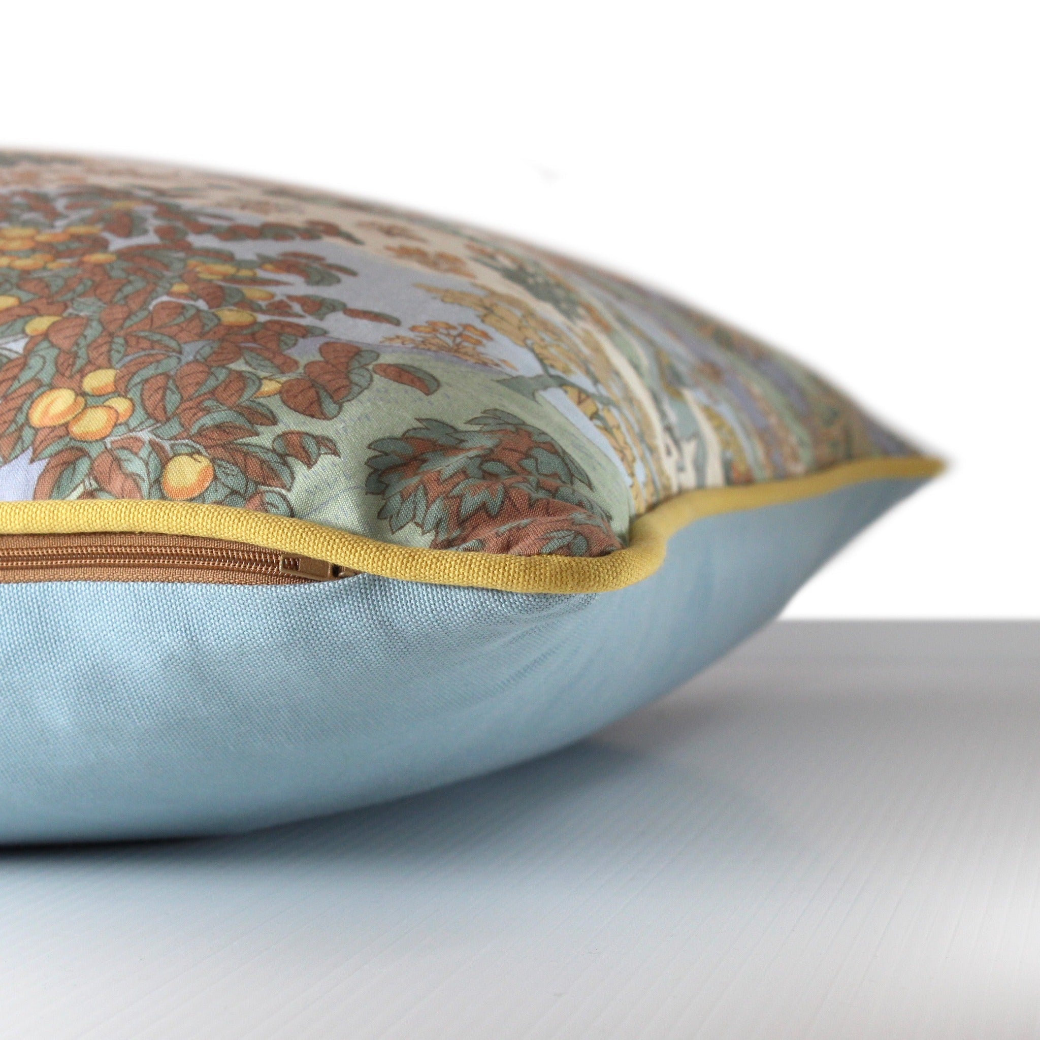 Side view of a cushion made from a vintage printed cotton with a Persian pictorial scene of riders in a forest in a colour palette of lemon, clementine, brown, mint. and powder blue