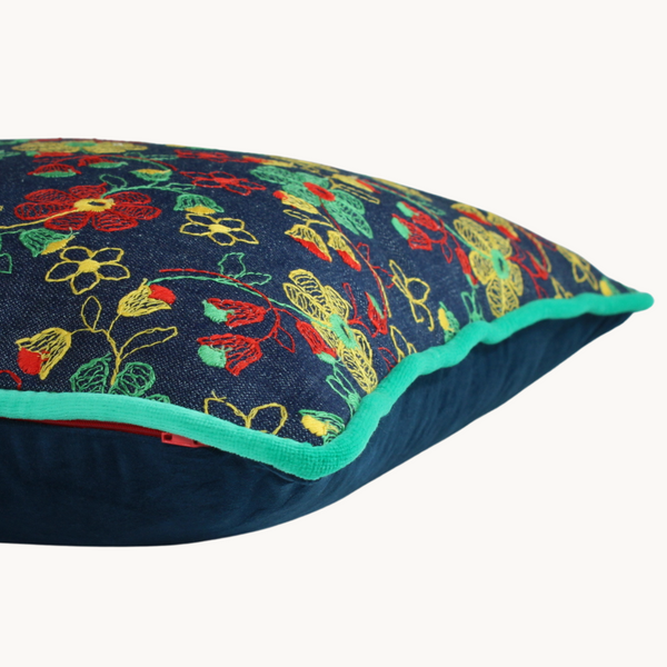 Side view of a vintage floral embroidered cushion, a denim base cloth with naive red, yellow and spearmint green flowers, yellow piping and an aqua cotton back