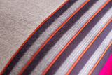 Close up of a striped fabric in grey, orange, aubergine and hot pink