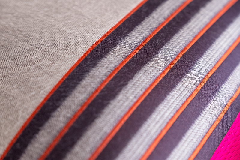 Close up of a striped fabric in grey, orange, aubergine and hot pink