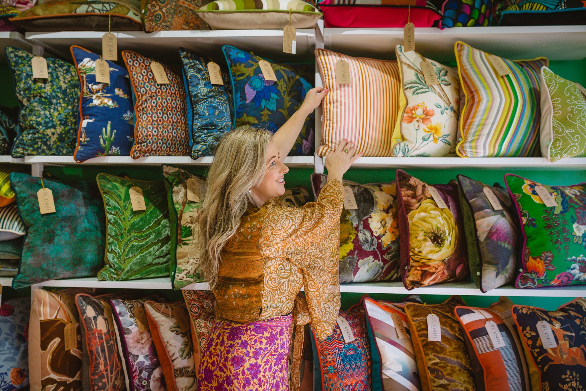 Woman shopping for decorative pillows in a store with a wide selection of colorful pillows.