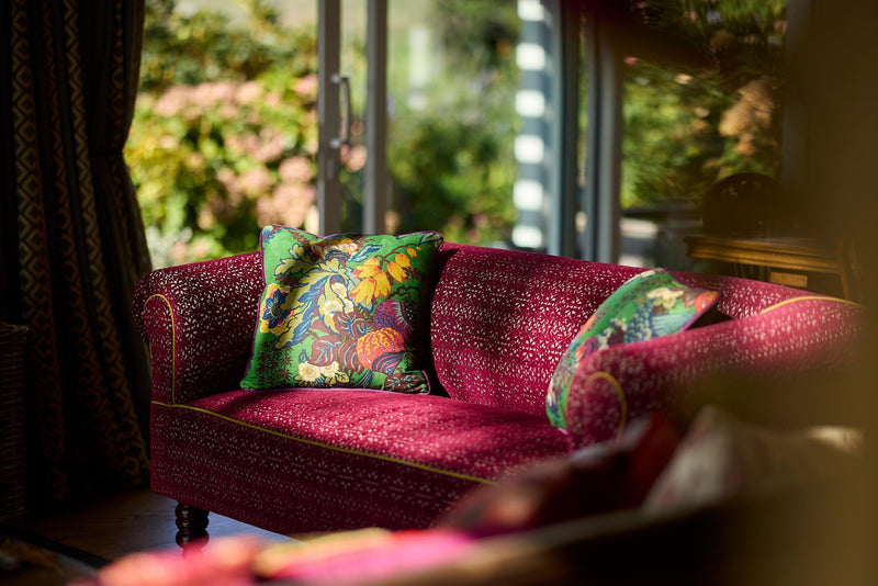 Photo of a sofa upholstered in berry coloured cut velvet with a vibrant emerald green floral linen cushion