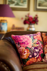 Close up of a sumptious velvet floral cushion in rich warm tones on a brown leather sofa.
