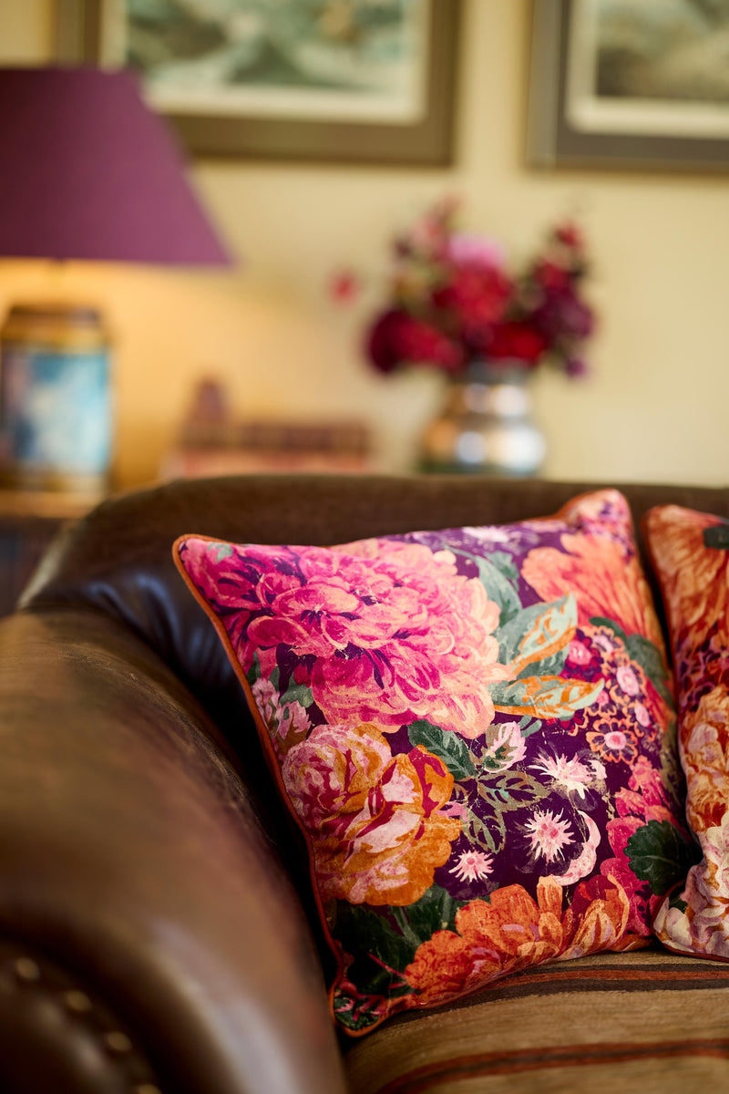 Close up of a sumptious velvet floral cushion in rich warm tones on a brown leather sofa.