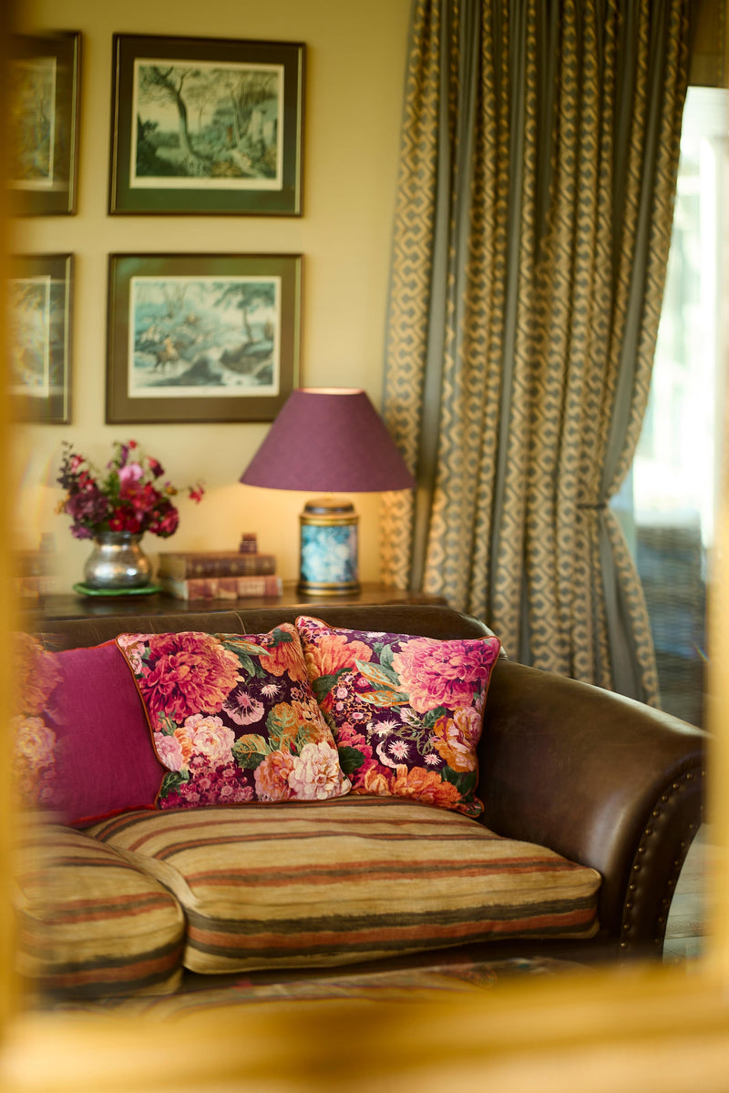 Photograph of a brown leather sofa with vibrant floral velvet cushions