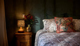 Photo of a moody bedroom setting with murky turquoise wallpaper, timber bedsides and a salmon coloured floral linen cushion