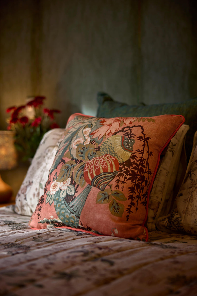 Close up photo of a salmon coloured floral linen cushion in a moody bedroom setting