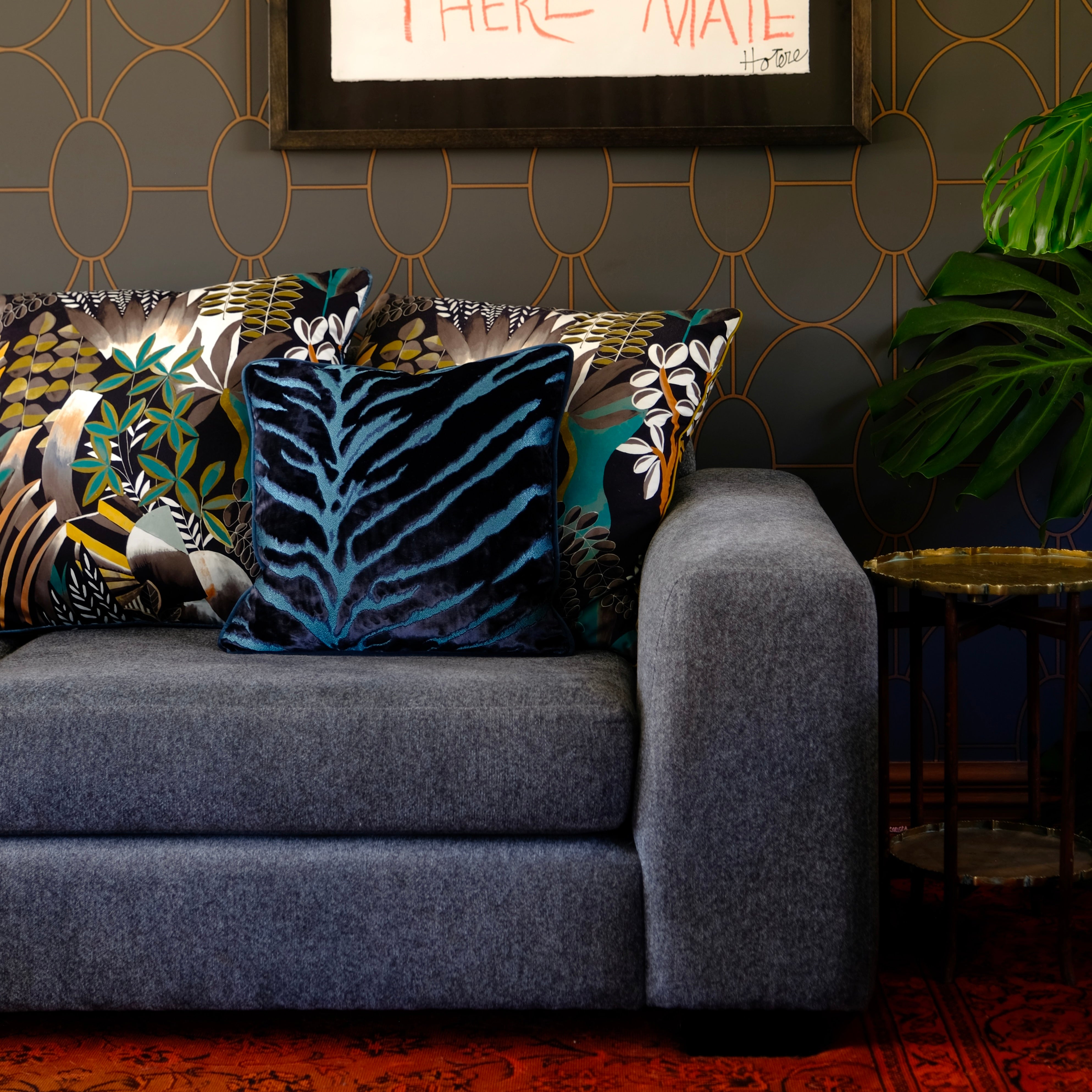 Gray sofa with patterned cushions against a dark wall with decorative gold patterns
