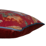 Side shot of a linen cushion in a rich red with blue and green large scale scrolled design