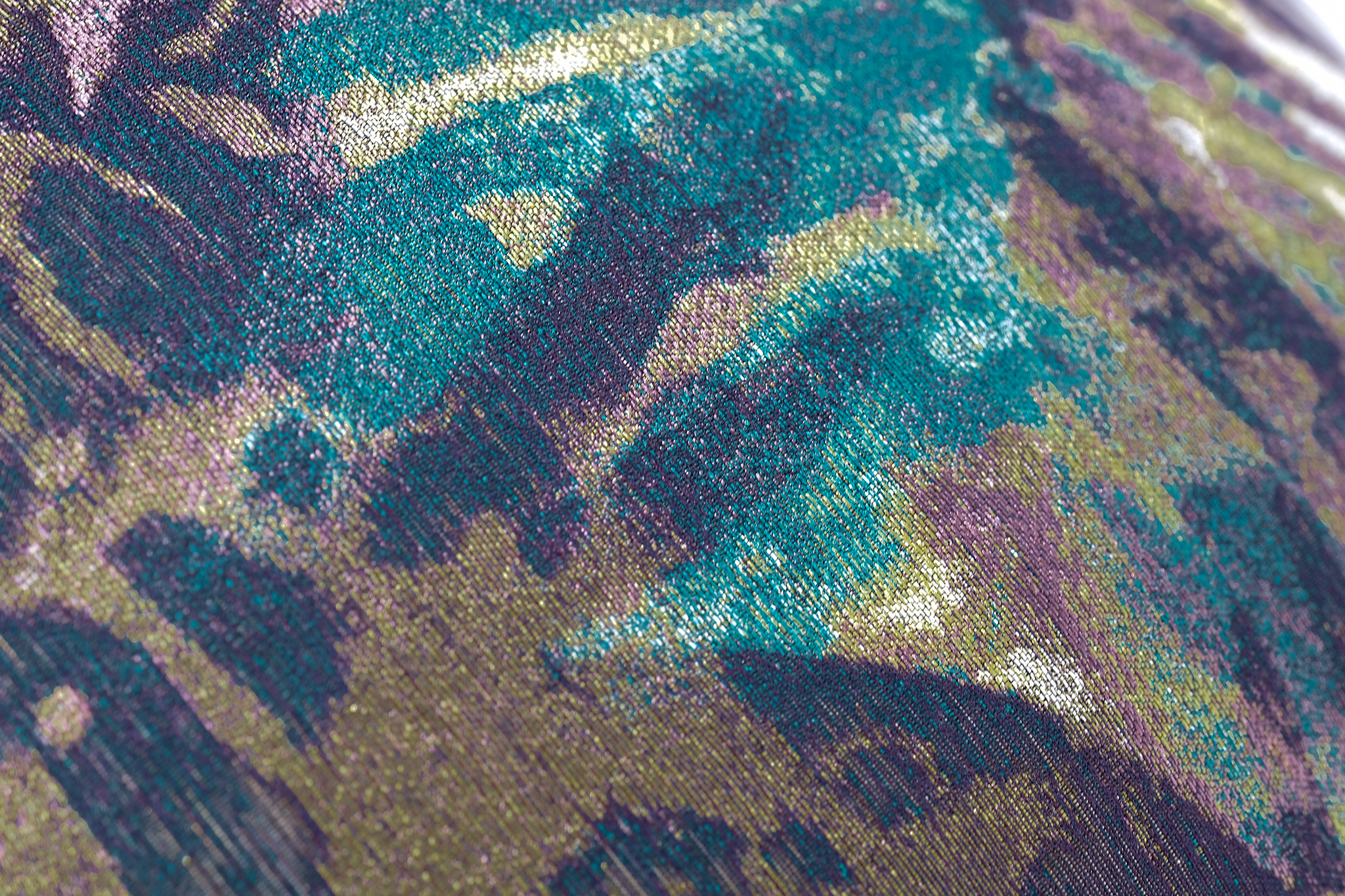 A close-up of a textured fabric with an abstract, painterly pattern in teal, purple, olive green, and black.