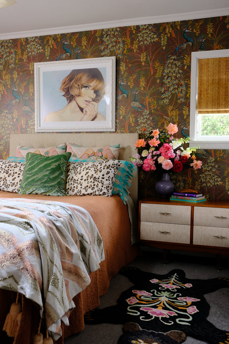 Decorative room interior with floral arrangement, framed picture, and patterned textiles.