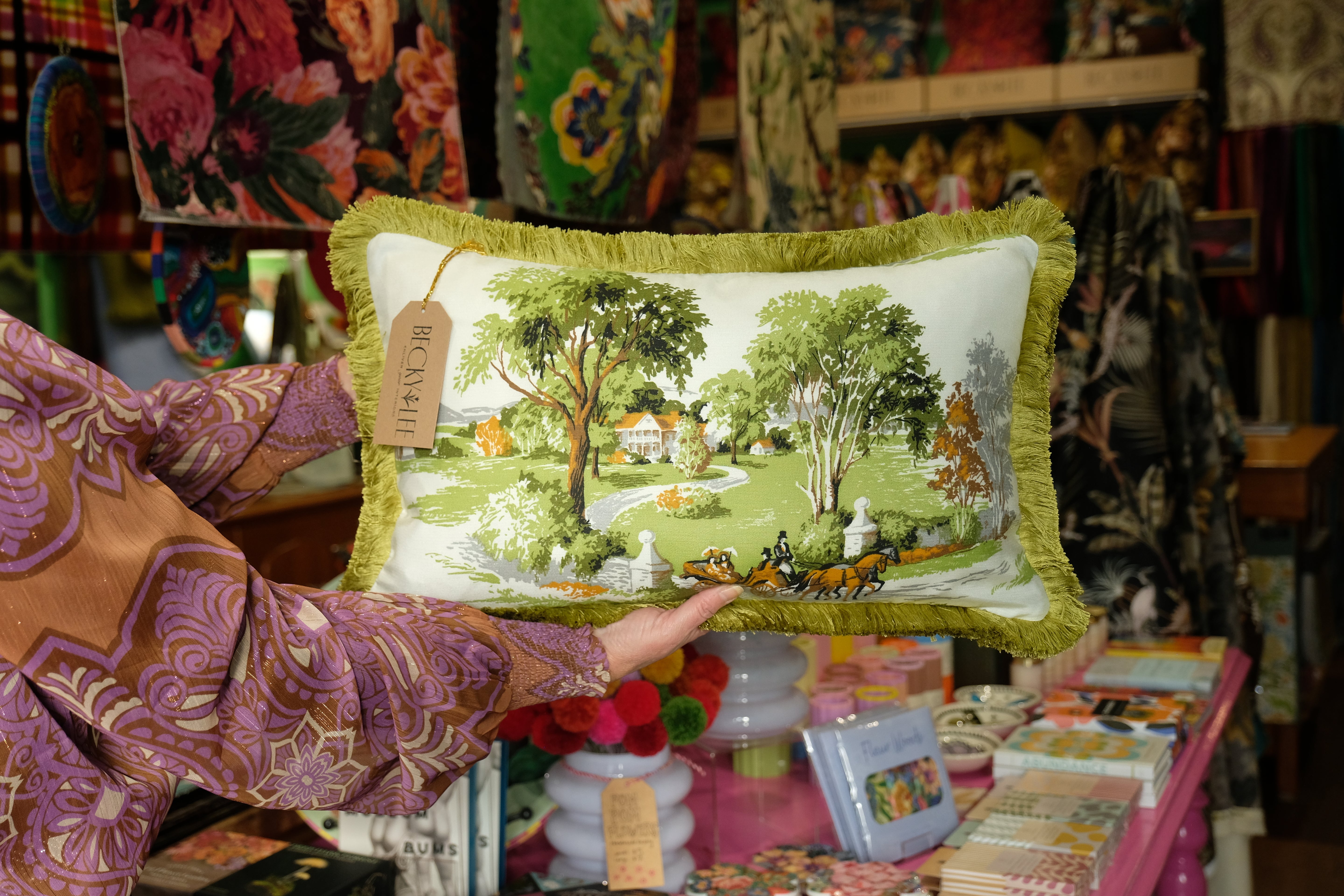Decorative pillow with a scenic design held by a person in a colorful setting.