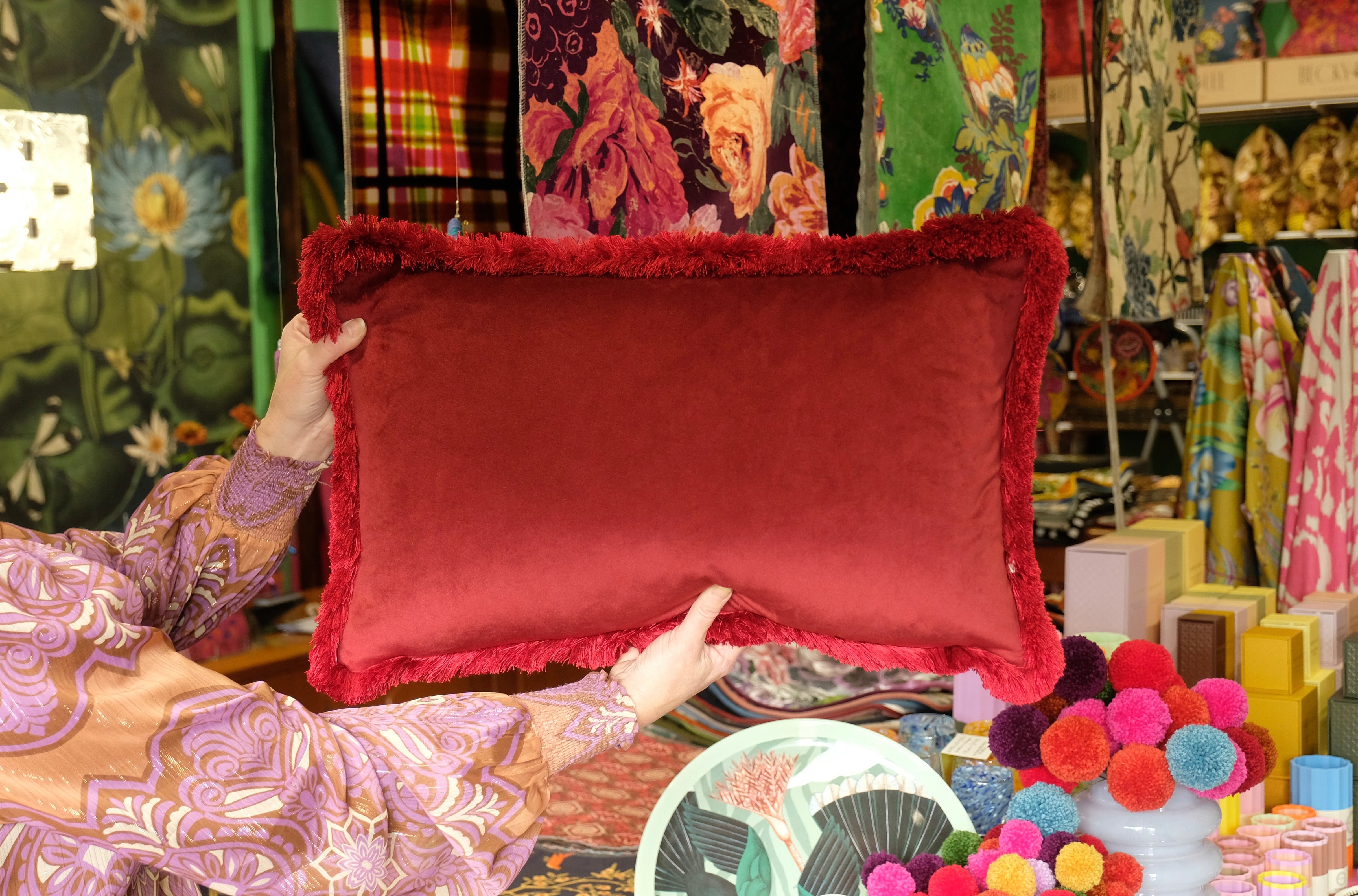 Person holding a red pillow in a colorful store setting with various items and patterns.