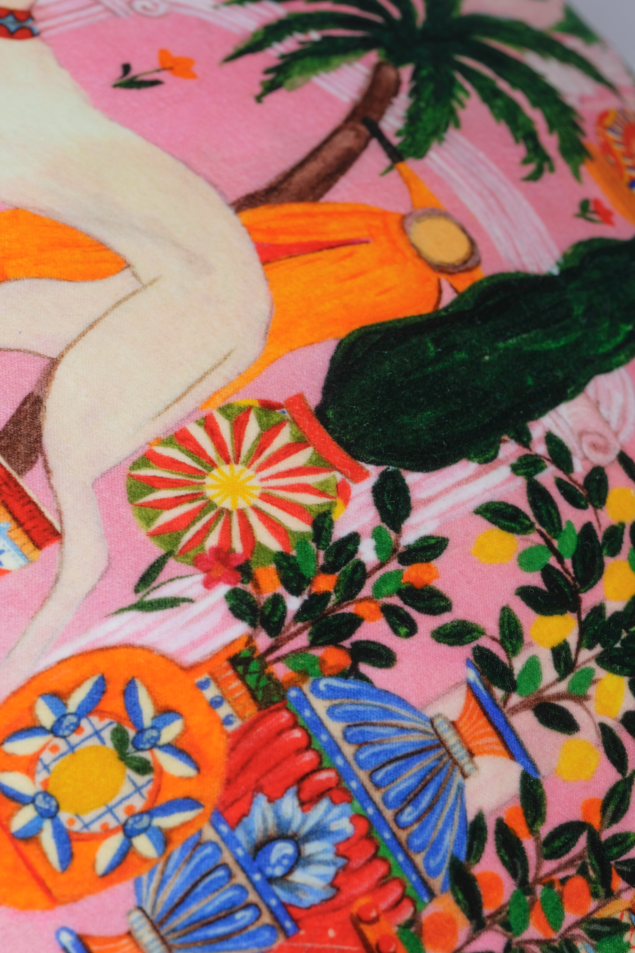 A close-up of a colorful printed textile featuring a pink background with illustrated tropical elements, including palm trees, flowers, and abstract shapes in orange, blue, green, yellow, and cream.