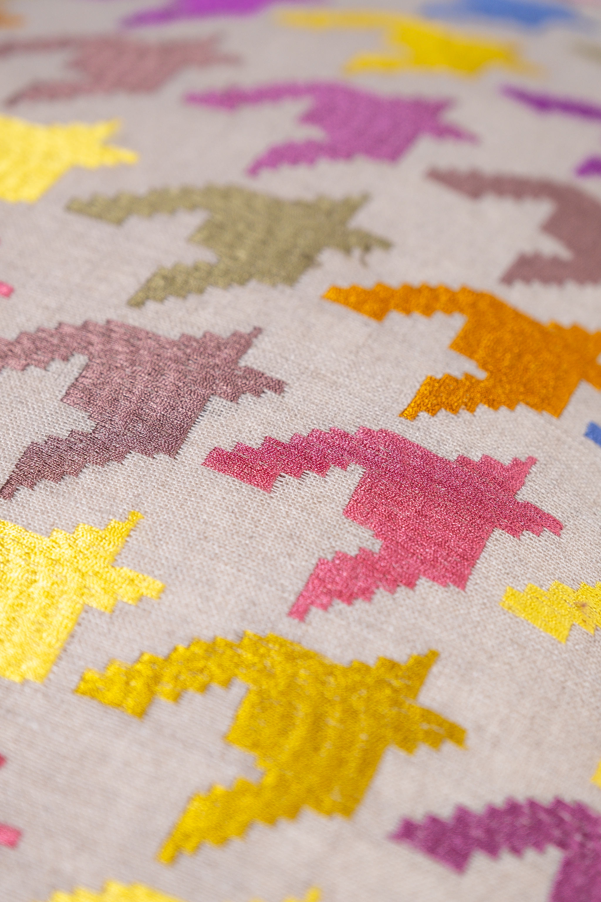Close up of an embroidered houndstooth pattern in purple gold and orange on a natural linen base