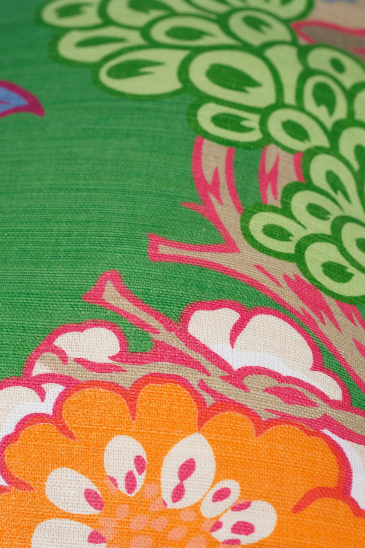 A close-up of a colorful patterned fabric featuring a bright green background with stylized orange, pink, and cream floral and leaf motifs.