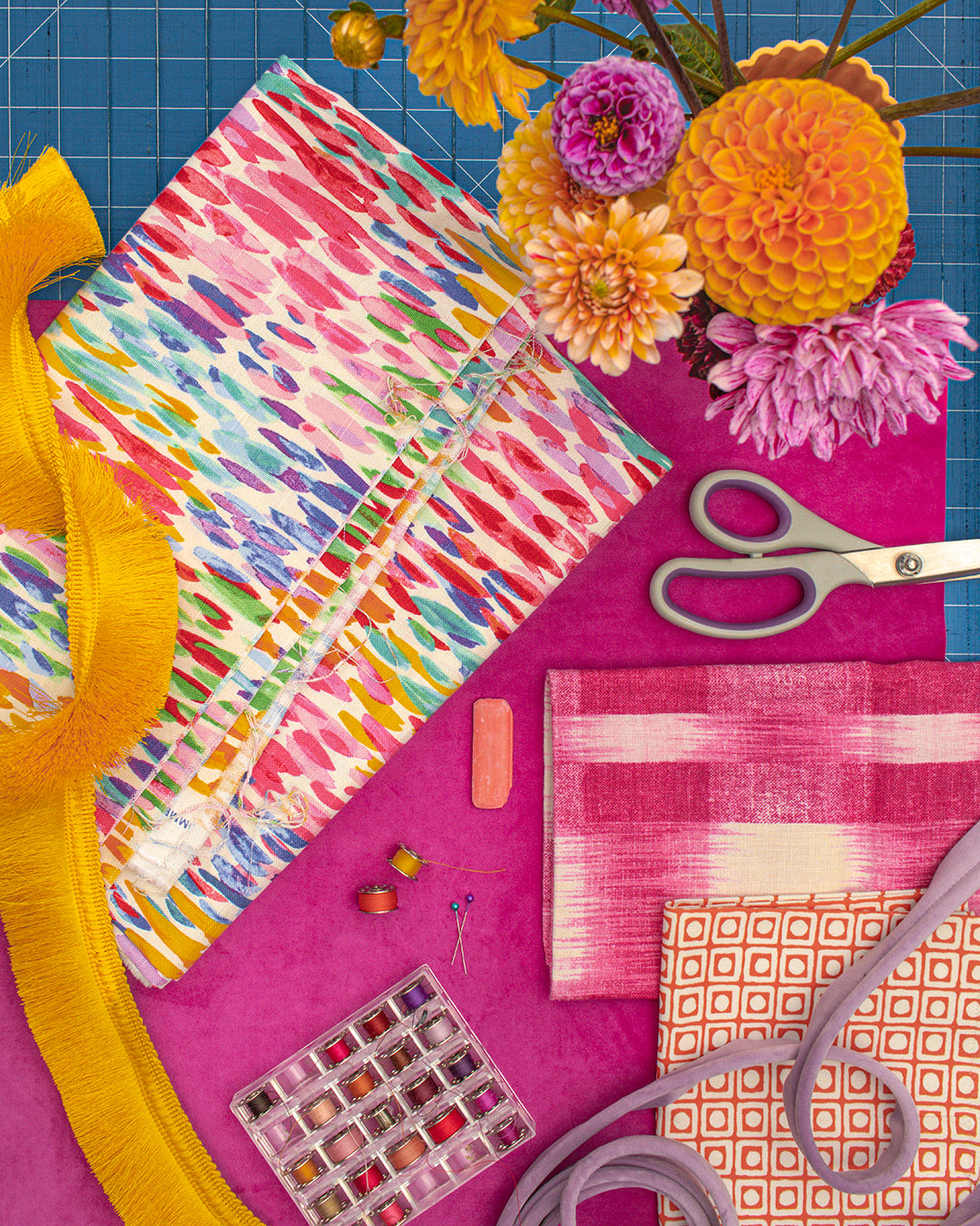 Colorful fabric with flowers, scissors, and sewing tools on a pink surface