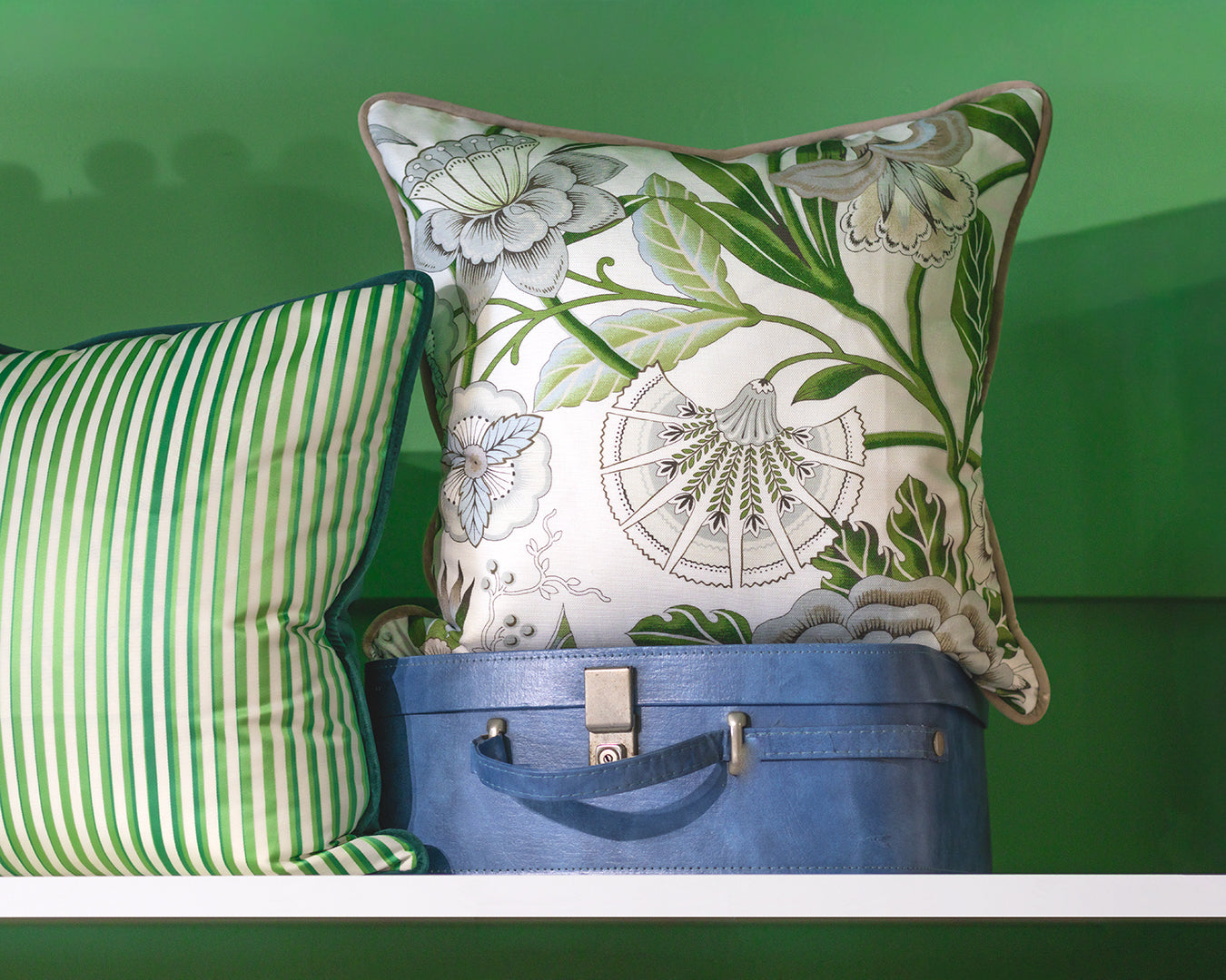 Two decorative pillows with green and white patterns on a blue suitcase against a green background