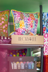 Colorful cushion with a 'Becky Lee' tag on a shelf with other decorative items.