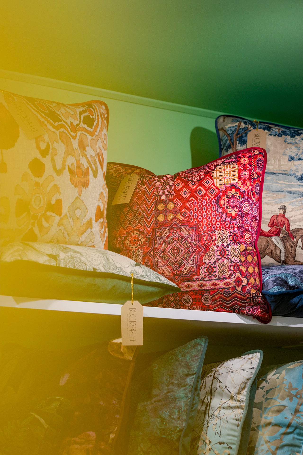 Colorful patterned pillows on a shelf with a green wall background