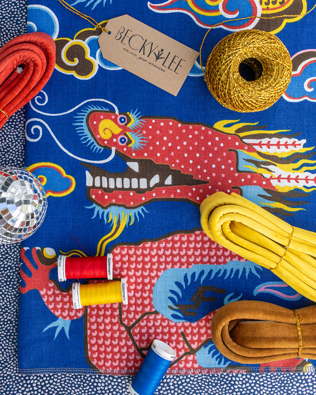 Colorful fabric with dragon design, sewing supplies, and a Becky Lee label.