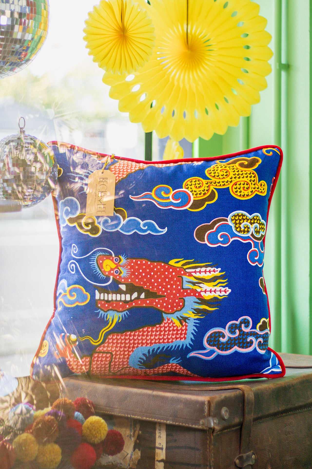 Decorative pillow with dragon design on an old leather suitcase with yellow fans in the background