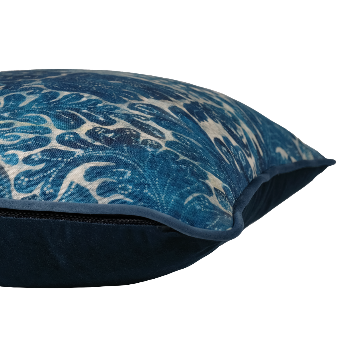 A close-up of a decorative throw pillow featuring a blue and cream wave pattern on the front cover and a solid navy blue velvet-like fabric lining and piping.