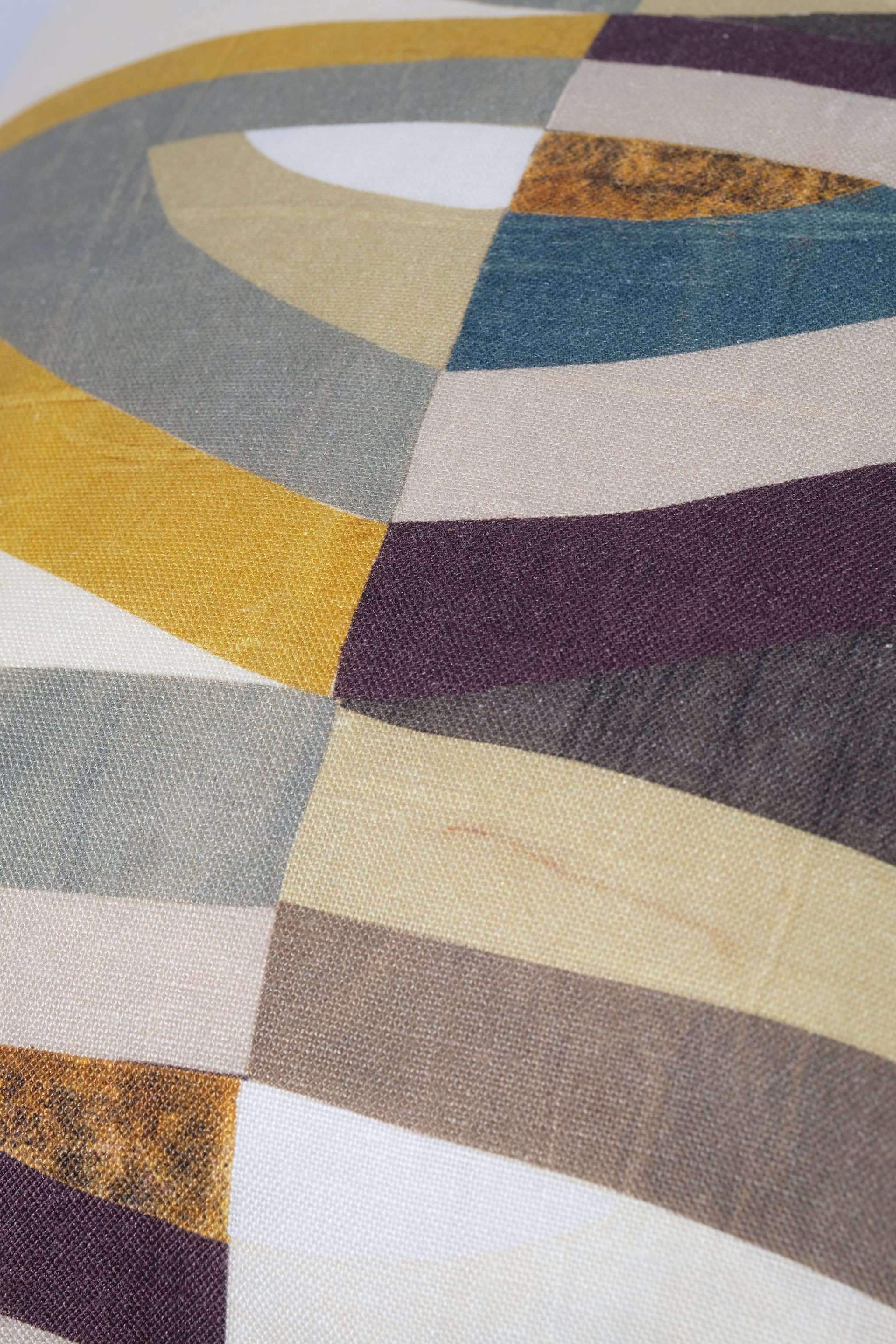 A close-up of a geometric patterned fabric with curved stripes in mustard yellow, slate blue, cream, dark purple, taupe, and white, showing a visible linen-like texture.