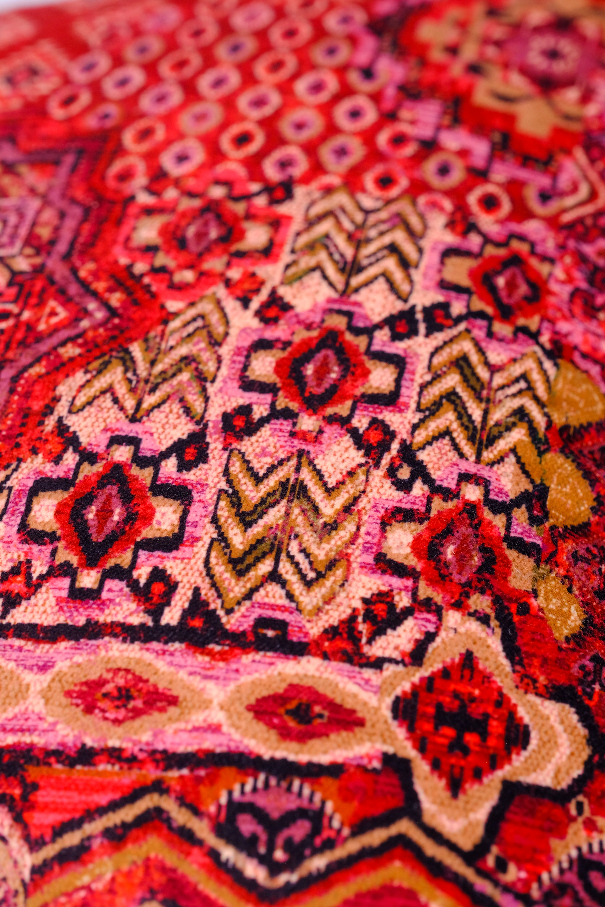 Close-up of a vibrant, patterned Persian velvet fabric with red, pink, and beige colors.