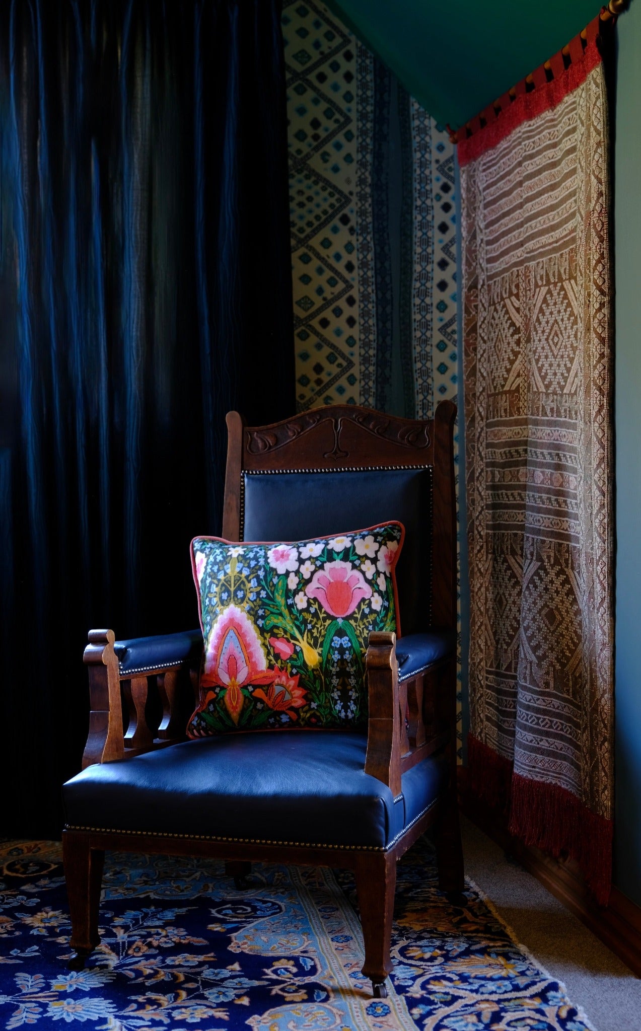 Maximalist corner in a room with a brightly coloured cushion sitting on a vintage wooden chair