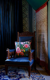 Maximalist corner in a room with a brightly coloured cushion sitting on a vintage wooden chair