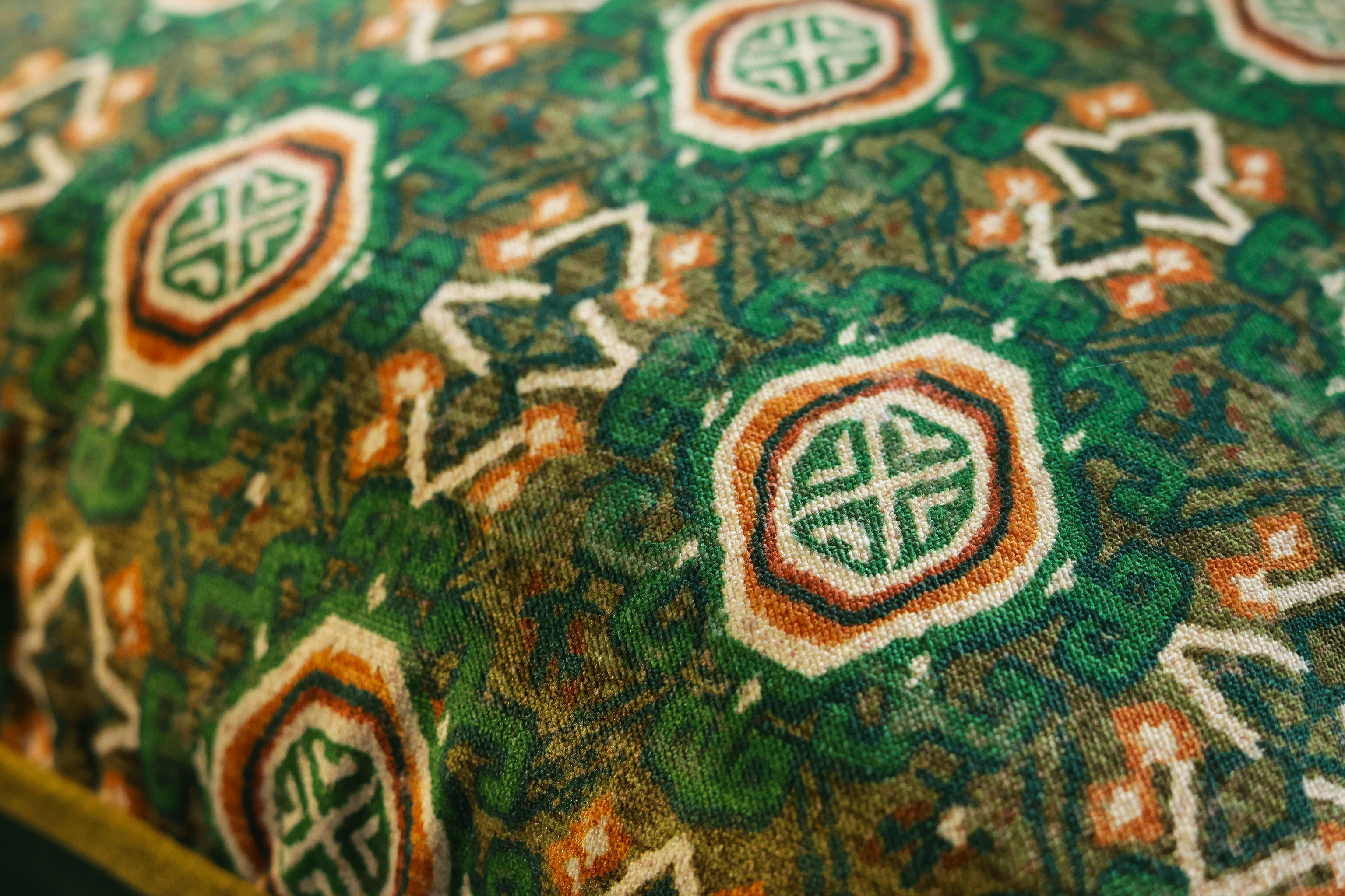 Close-up of a patterned textile with repeating octagonal medallion motifs in green, orange, white, and brown tones.