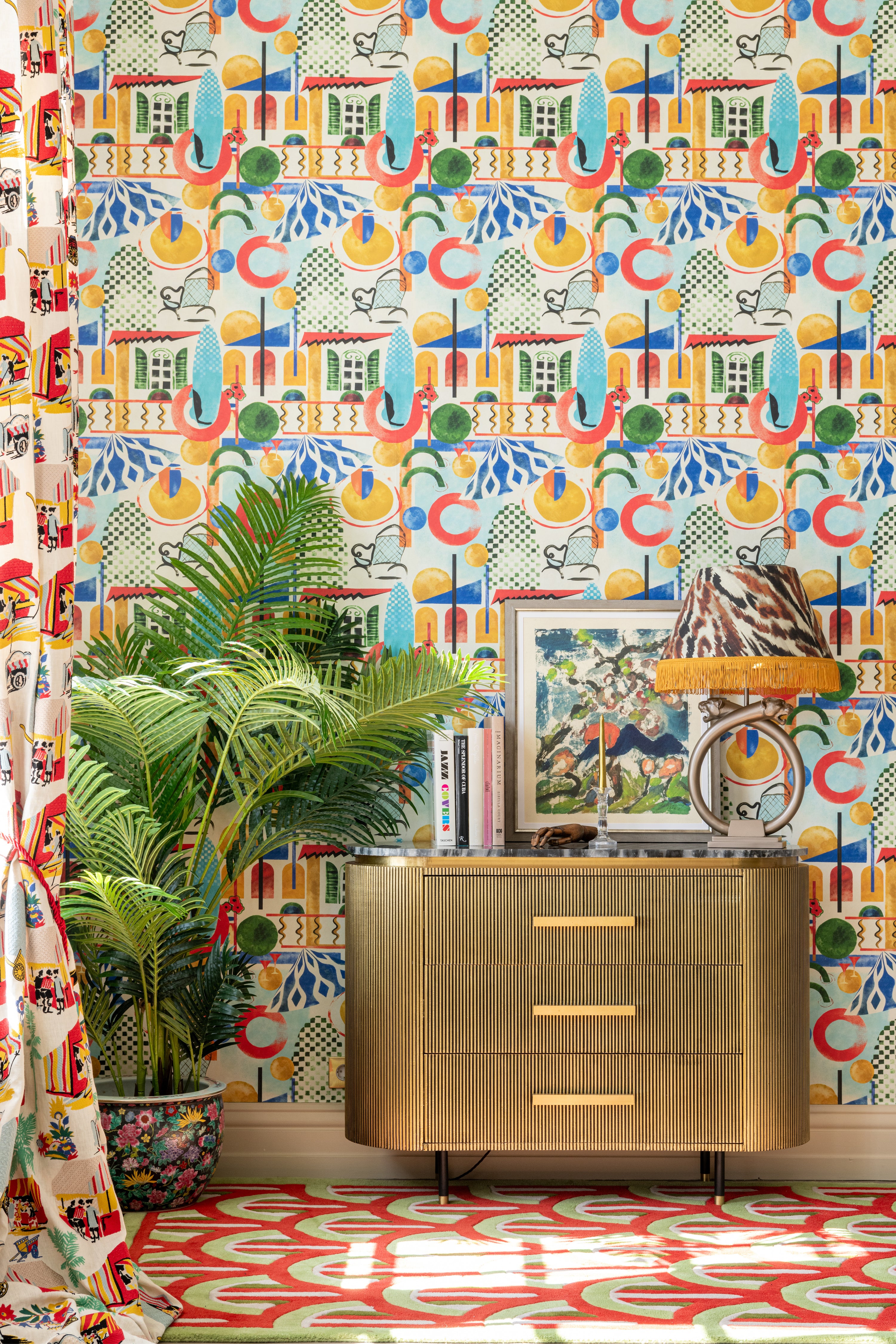 
A stylish room with Mind The Gap Veranda wallpaper, a dark wood sideboard, golden accents, potted palm, and framed art creating a sophisticated look