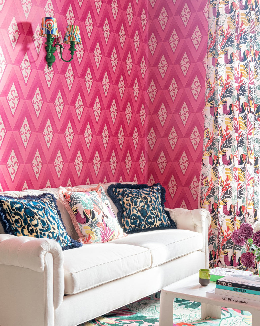  bright pink diamond-patterned wallpaper complements a chic living room with a white couch, patterned cushions, and floral curtains