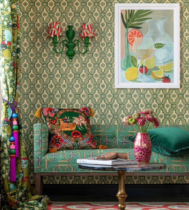 A vibrant living room with Palloncini Verde wallpaper, a green patterned sofa, bold cushions, floral décor, and a framed citrus-inspired painting