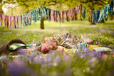 Photo of a large colourful pile of cushions in a woodland setting with fabric garlands strung in the trees