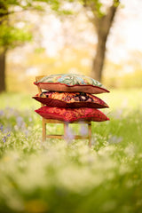 Photo of three colourful patterned cushions stacked on a Bentwood chair in a woodland setting