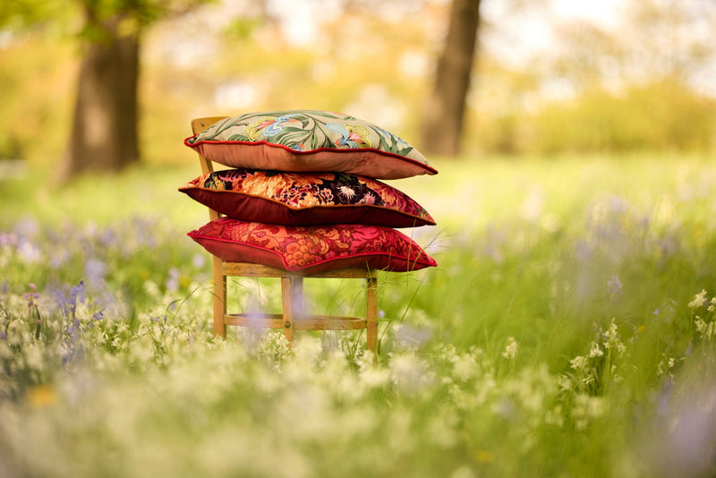 Photo of three colourful warm coloured cushions stacked on a Bentwood chair in a woodland setting