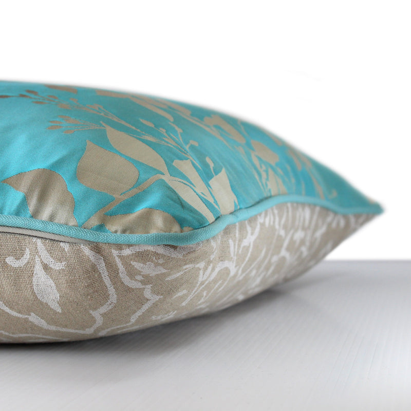 Side view of a silk blend cushion in a luminous aqua ombre with sand coloured leaves and aqua cotton piping